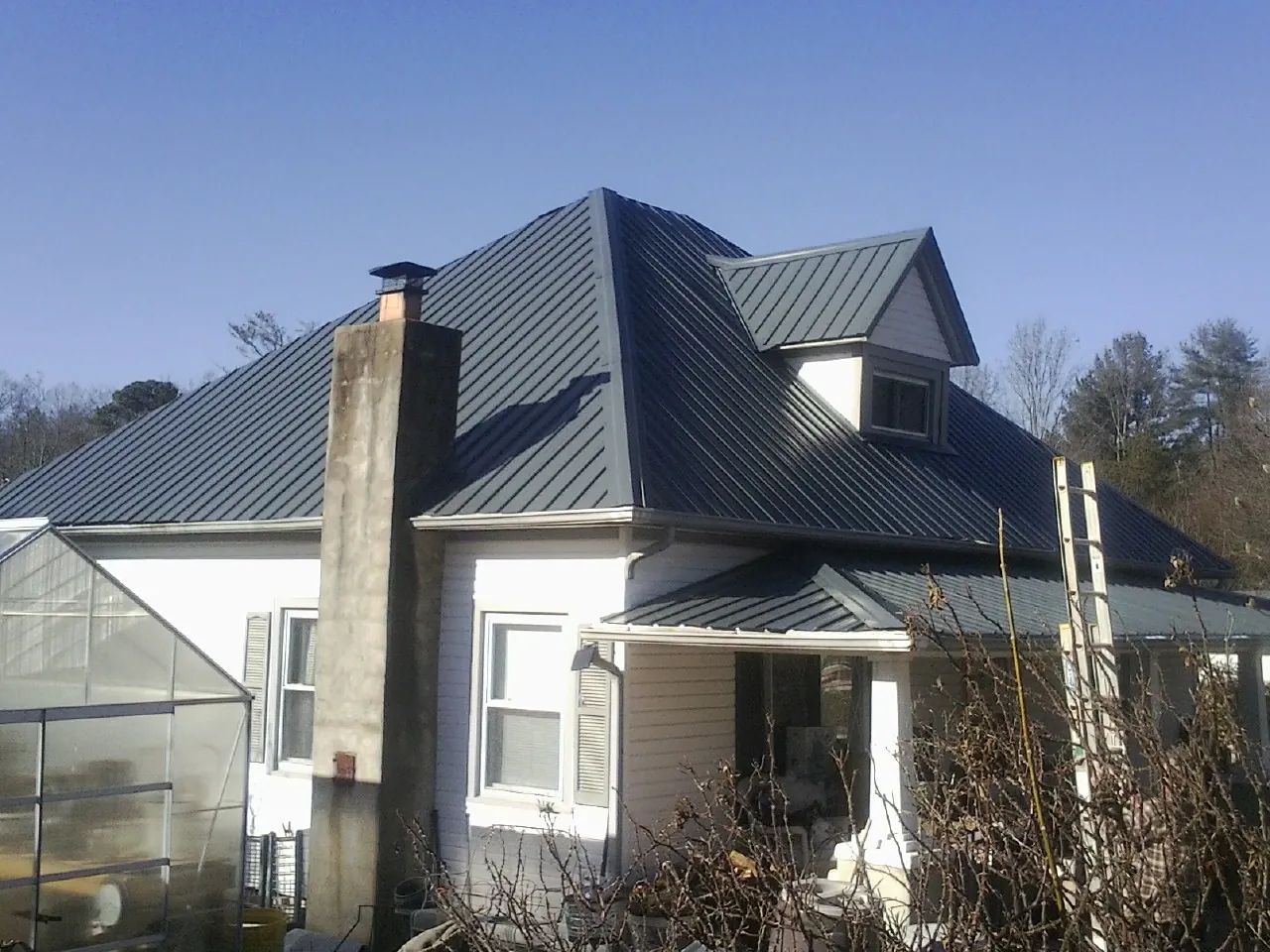 Dark blue standing seam metal roof on a white farmhouse with dormer — Slate & Tile Roof Repair by Roofing Brothers in Tensed