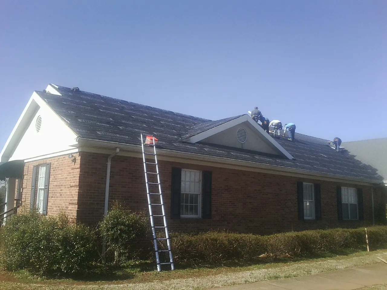 Crew tearing shingles off a brick ranch roof with a ladder set — Metal Roof Repair work by our crew in Tensed