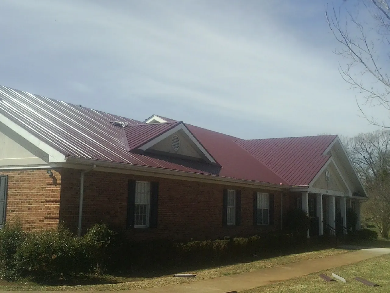 Red metal roof with gabled entries on a long brick building, from a Hail Damage Roof Repair job in Tensed