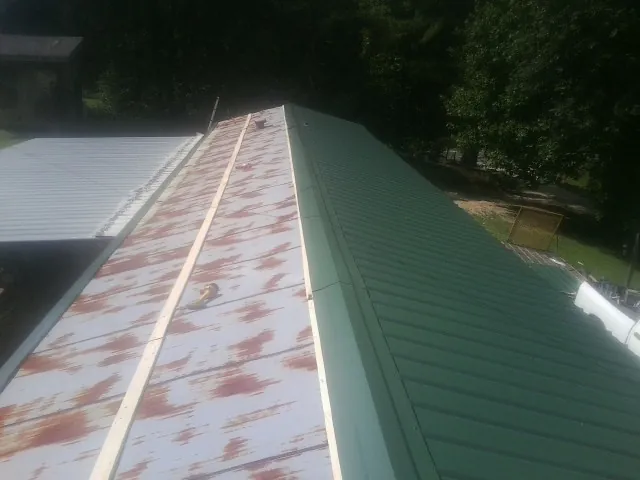 Old rusted panels beside newly installed green metal roofing — Wind Damage Roof Repair by Roofing Brothers in Tensed