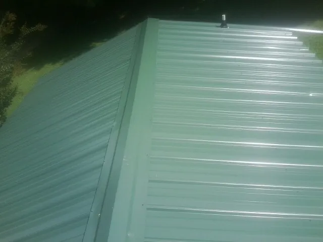 New green metal panels meeting at the ridge of a roof — Flat Roof Repair work by our crew in Tensed