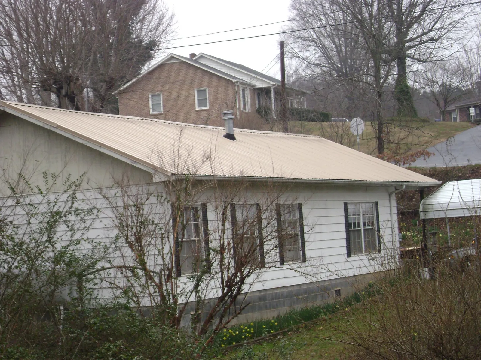 Tan metal roof on a white sided house set into a hillside — Commercial Roofing by Roofing Brothers in Tensed
